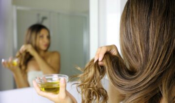 O femeie cu părul lung aplică o mască de păr dintr-un bol în care are ulei de măsline