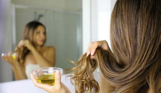 O femeie cu părul lung aplică o mască de păr dintr-un bol în care are ulei de măsline