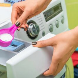 Femeie care adaugă detergent de spălat rufe în mașina de spălat
