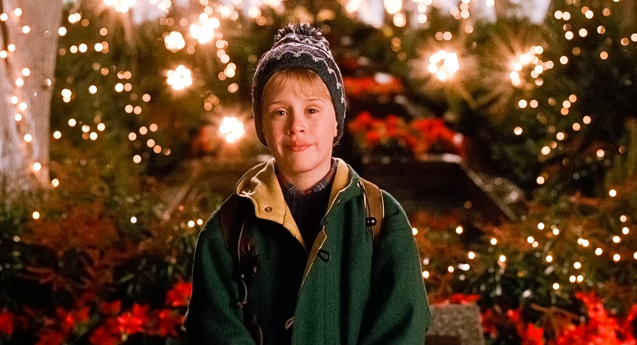 Macaulay Culkin în rolul principal din filmul Home Alone 2, îmbrăcat într-o geacă verde și fes pe cap.