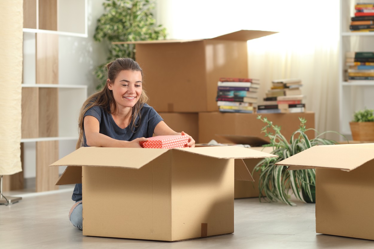 O femeie zâmbește în timp ce despachetează o cutie mare de carton, după ce s-a mutat singură