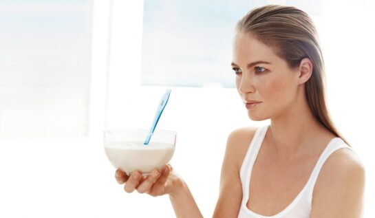 O femeie blondă cu ochi albaștri care ține în mână un bol cu iaurt și privește în zare
