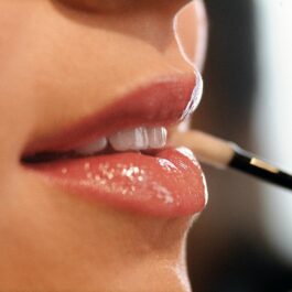 Cadru apropiat cu buzele unei femei, care aplică luciu de buze cu pensula