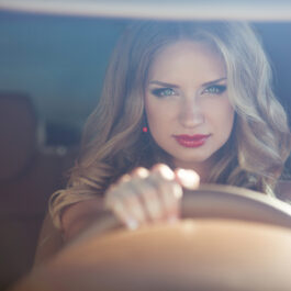 O femeie frumoasă și zâmbitoare pune mâna pe volanul mașinii pe care o conduce