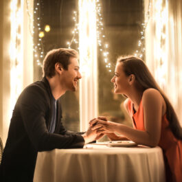 Un bărbat și o femeie stau la masa și se țin de mână