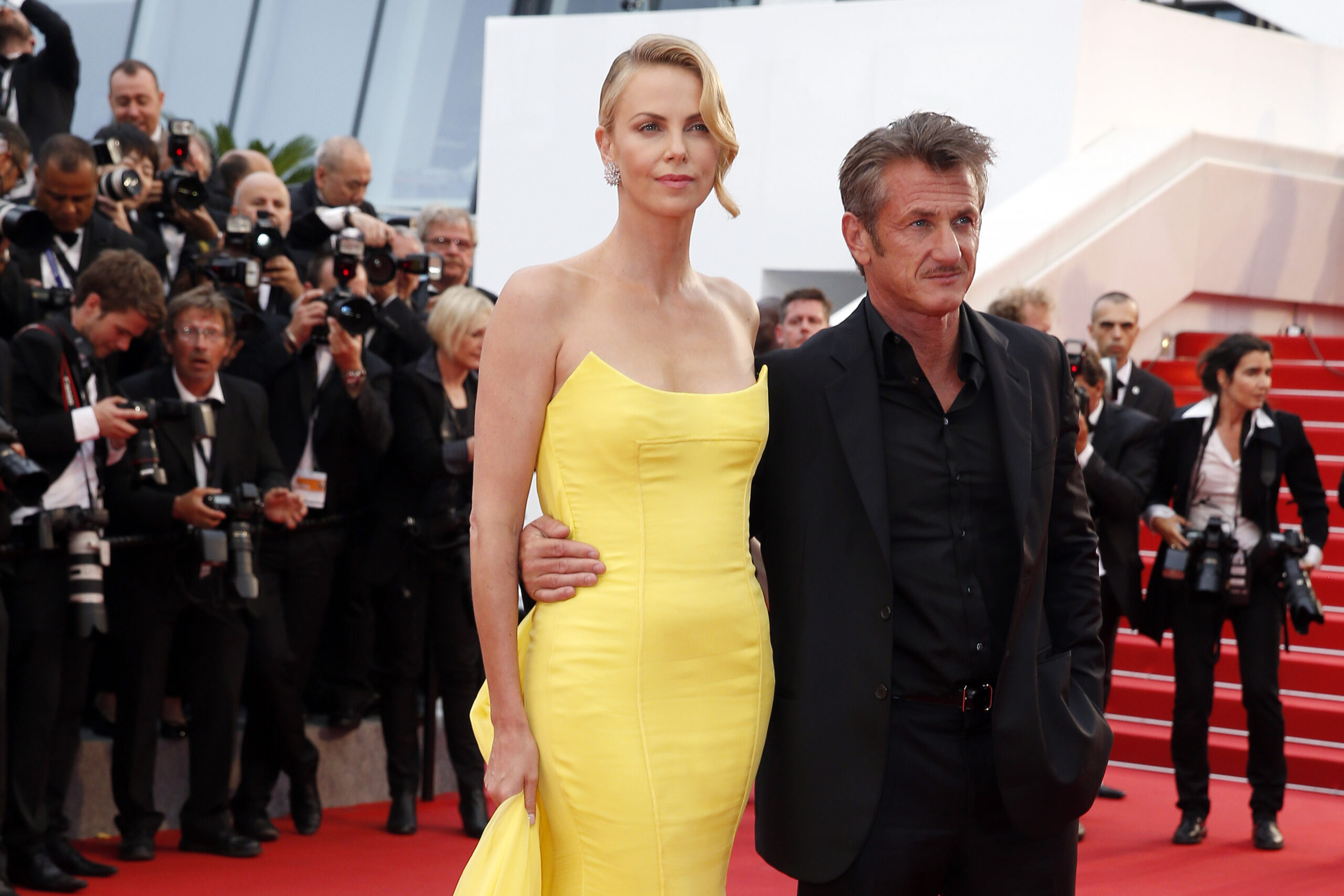 Charlize Theron pozează pe covoru roșu alături de Sean Penn îmbrăcată într-o rochie lungă, mulată și cu umerii goi