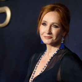 J. K. Rowling pozează pe covorul roșu îmbrăcată într-o rochie albastră, cu mărgele albastre la gât și cercei albaștri la urechi