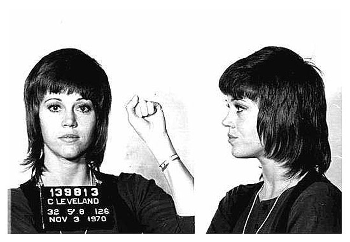 Fotografie alb-negru cu Jane Fonda la secția de poliție cu pumnul ridicat