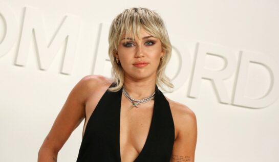 Miley Cyrus pozează îmbrăcată într-o rochi neagră cu decolteu adânc și o tusoare tip chică pe covorul roșu la prezentarea de modă Tom Ford