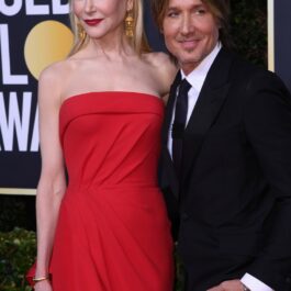 Nicole Kidman pozează într-o rochie roșie pe covorul roșu alături de Keith Urban îmbrăcat cu un costum negru elegant și cravata
