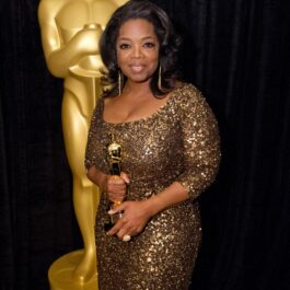 Oprah Winfrey este îmbrăcată într-o rochie aurie și ține în mână un trofeu Oscar