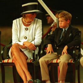 Prințesa Diana îmbrăcată ntr-un compleu alb elegant alcătuit din sacou și fustă participă la un eveniment alături de Prințul Harry îmbrăcat în pantaloni crem și sacou albastru