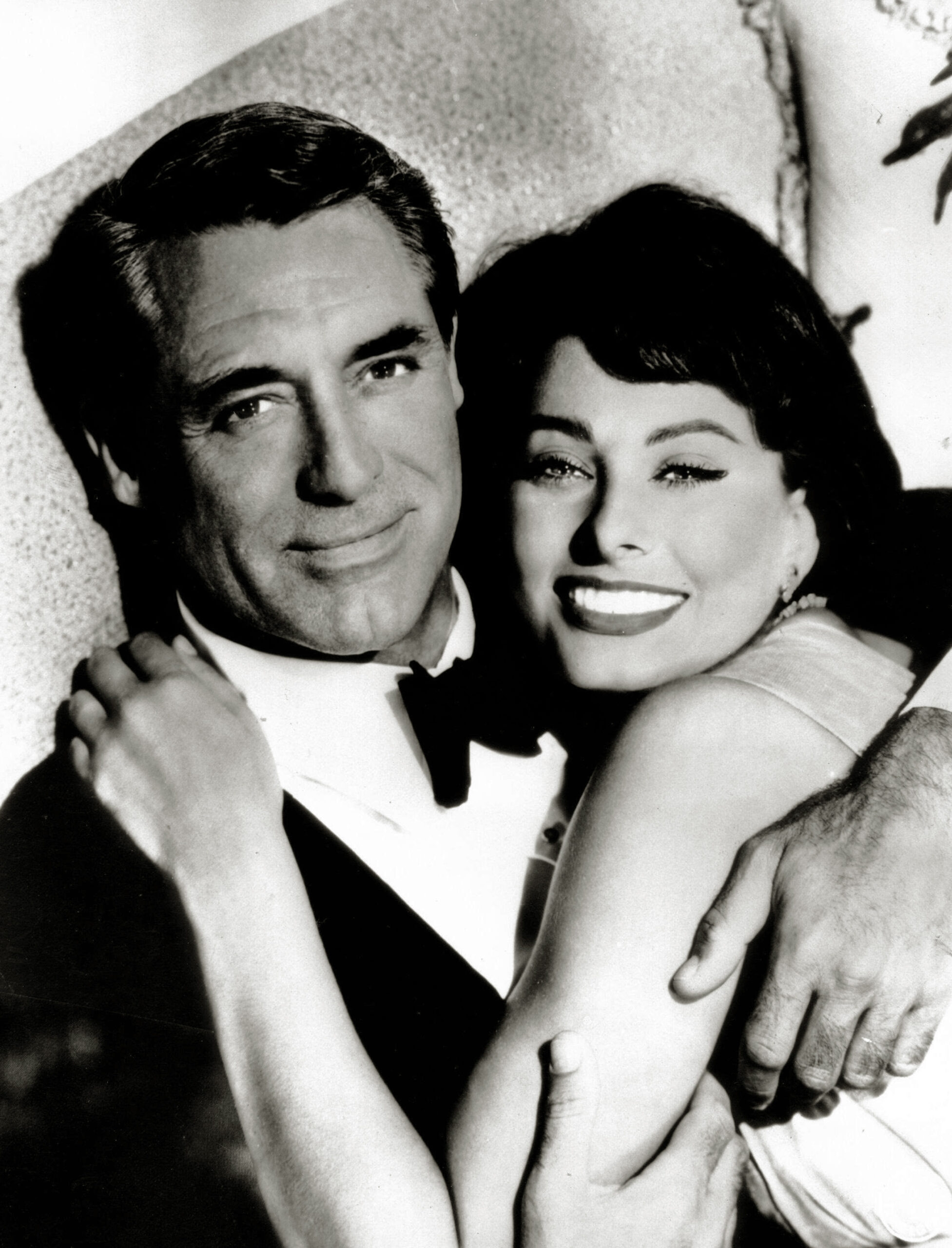 Fotografie alb-negru cu Sophia Loren îmbrățișânu-l pe Cary Grant pe o canapea