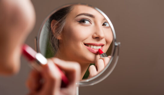 O femeie se uită în oglindă în timp ce aplică ruj roșu pe buze