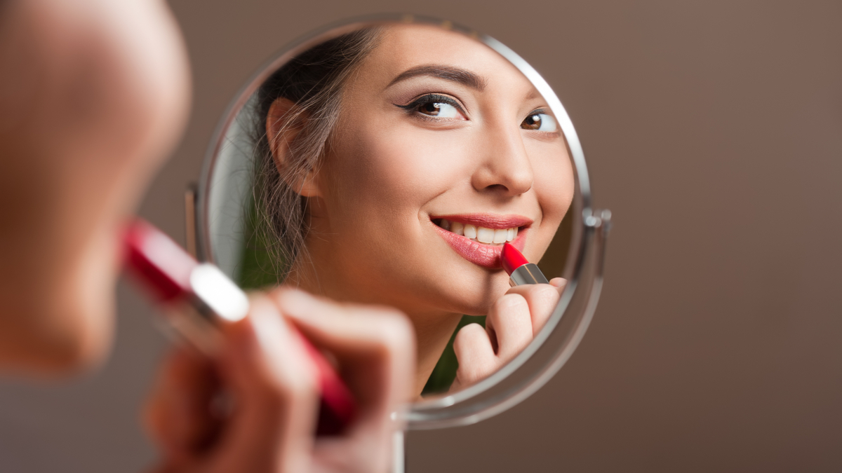 O femeie se uită în oglindă în timp ce aplică ruj roșu pe buze