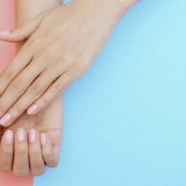 Două mâini cu manichiură transparentă pe un fundal albastru și roz