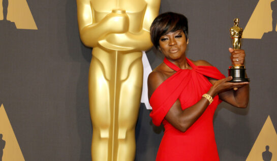 Viola Davis îmbrăcată într-o rochie roșie țină în mână o statuetă Oscar