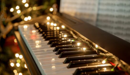 Un pian, pe care e așezată o instalație de brad și o partitură cu piese de Crăciun.