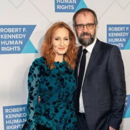 J. K. Rowling pozează pe covorul roșu alături de soțul ei. Ea poartă o rochie albastră și el un costum albastru