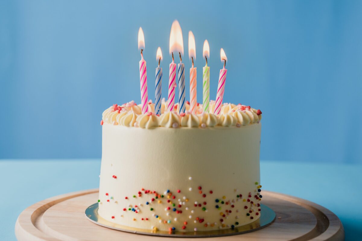 Tort cu cremă albă, decorat cu bomboane multicolore și lumânări pentru a sărbători o zi de naștere.