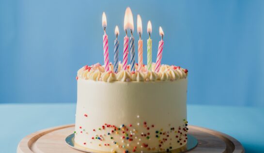 Tort cu cremă albă, decorat cu bomboane multicolore și lumânări pentru a sărbători o zi de naștere.