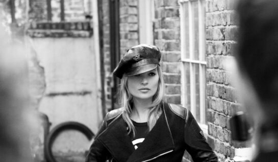 Fotografie alb-negru cu Kate Moss în care modelul poartă o șapcă elegantă și o geacă neagră de piele