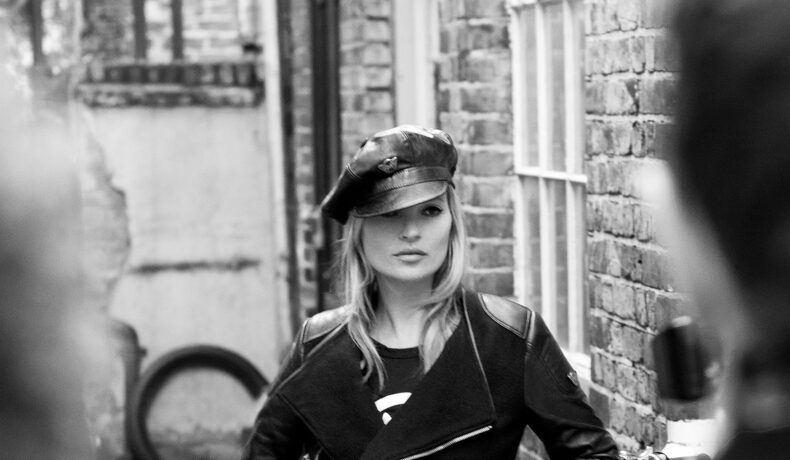 Fotografie alb-negru cu Kate Moss în care modelul poartă o șapcă elegantă și o geacă neagră de piele