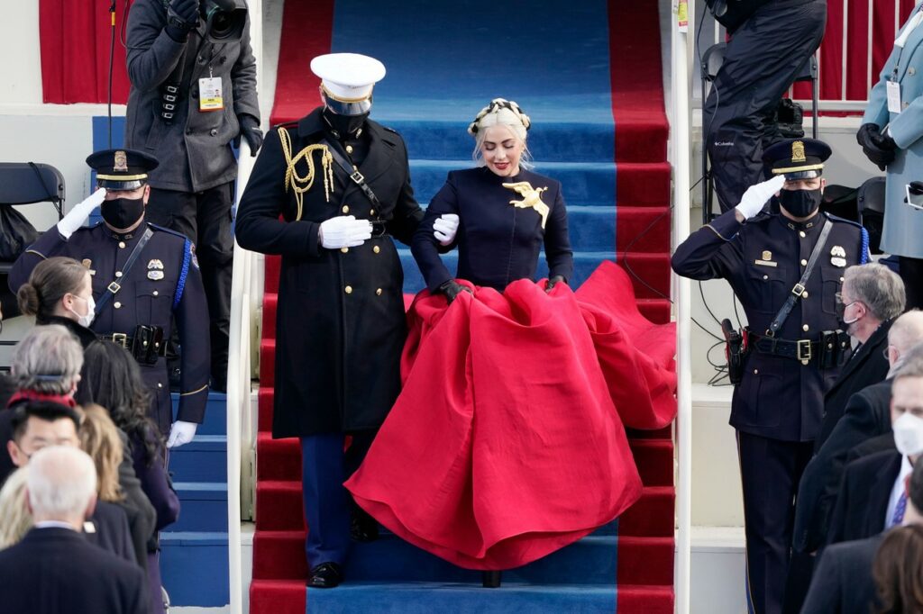 Lady Gaga apare la Casa Albă însoțită la braț de un militar. Este îmbrăcată cu o fustă roșie și un sacou negru