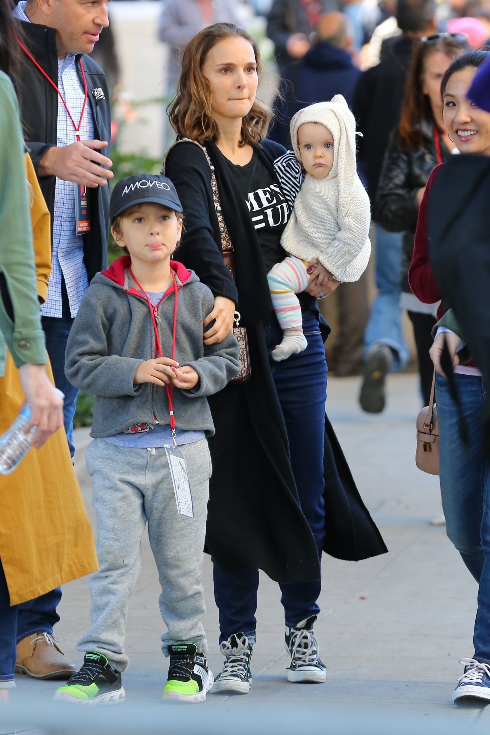 Natalie Portman o ține în brațe pe fiica ei Amalia îmbrăcată cu un costum alb și îl atinge pe umăr pe fiul ei Aleph îmbrăcat cu un training