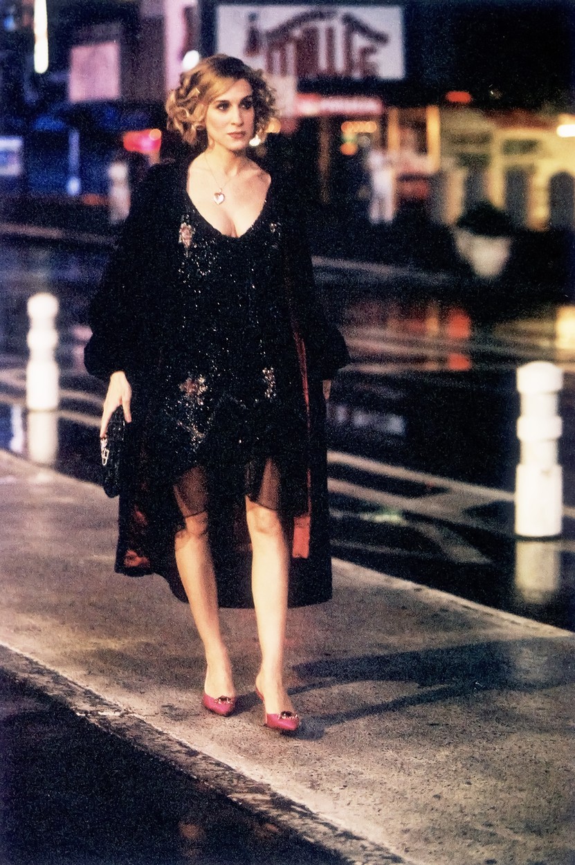 Sarah Jessica Parker îmbrăcată cu o rochie neagră strălucitoare și sex, o haină de blană și tocuri pe străzile New Yorkului