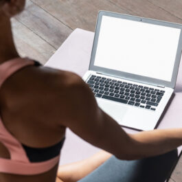 O femeie îmbrăcată cu o bustieră sport și colanți stă într-o poziție de yoga în fața unui laptop