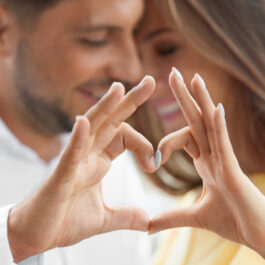 Un bărbat și o femeie se îmbrățișează și își țin mâinile în forma unei inimi