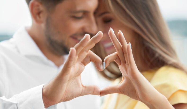 Un bărbat și o femeie se îmbrățișează și își țin mâinile în forma unei inimi
