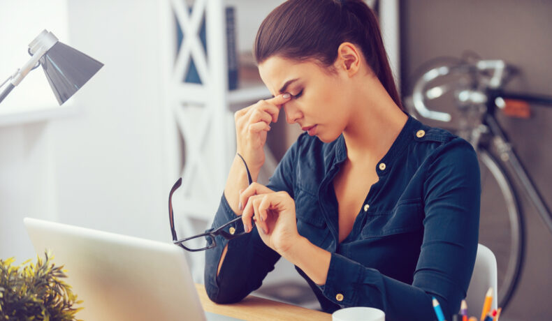 O femeie stă la birou șși își masează fruntea