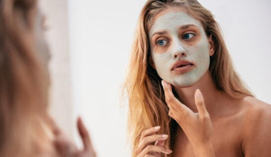 O femeie tânără cu părul lung și blond se uită în oglindă după ce și-a aplicat pe față o mască
