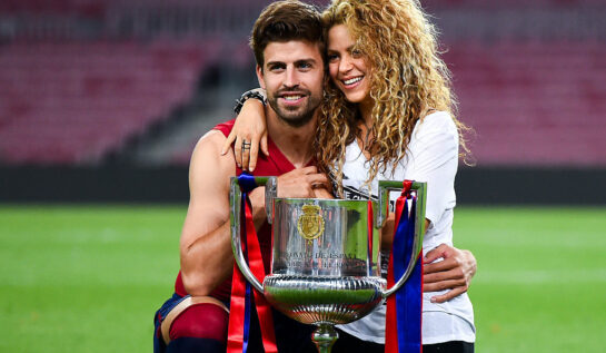 Shakira îl îmbrățișează pe Gerard Pique pe terenul de fotbal. În fața lor este o cupă de fotbal