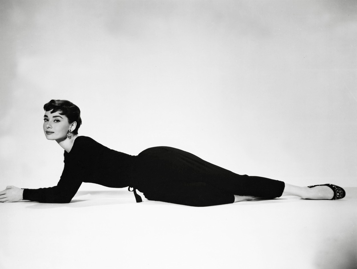 Poză alb-negru cu Audrey Hepburn încălțată cu balerini negri șă îmbrăcată într-o ținură neagră