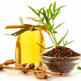 Un recipient din sticlă care conține ulei de susan și câteva frunze verzi. În fața lui se află un bol cu semințe de susan uscate.
