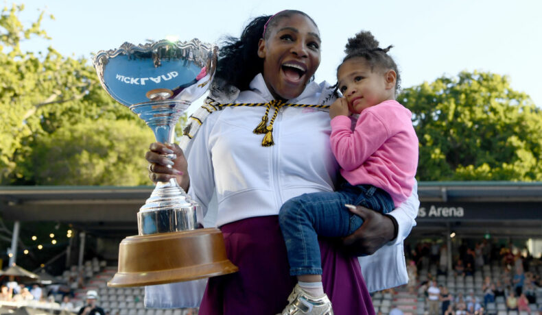 Serena Williams și fiica ei pe terenul de tenis, în timp ce ține în mână trofeul câstigat