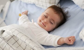 Un bebeluș zâmbește și își întinde brațele în timpul somnului