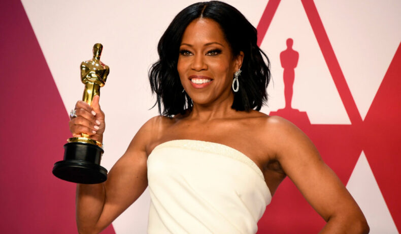 Regina King pe covorul roșu la Oscar cu o statuetă în mână, îmbrăcată cu o rochie albă fără bretele