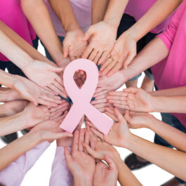 Mai multe mâini de femei într-un cerc țin o panglică roz
