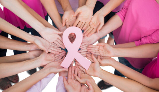 Mai multe mâini de femei într-un cerc țin o panglică roz