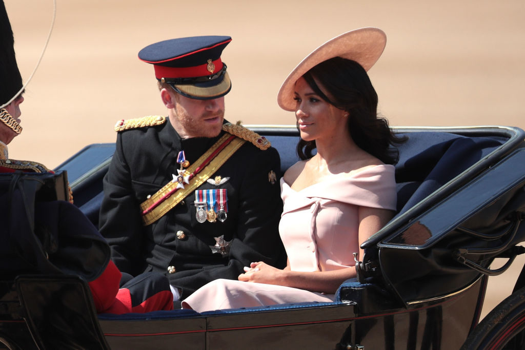 Meghan Markle în caleașcă alături de Prințul Harry îmbrăcată cu o rochie roz cu umerii goi și o pălărie roz