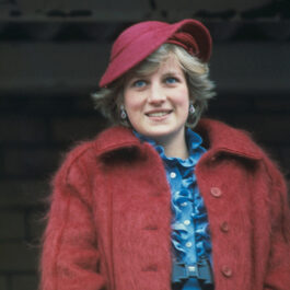 Prințesa Diana cu o pălărie burgundi pe cap, cu o bluză albastră și o haină cărămizie