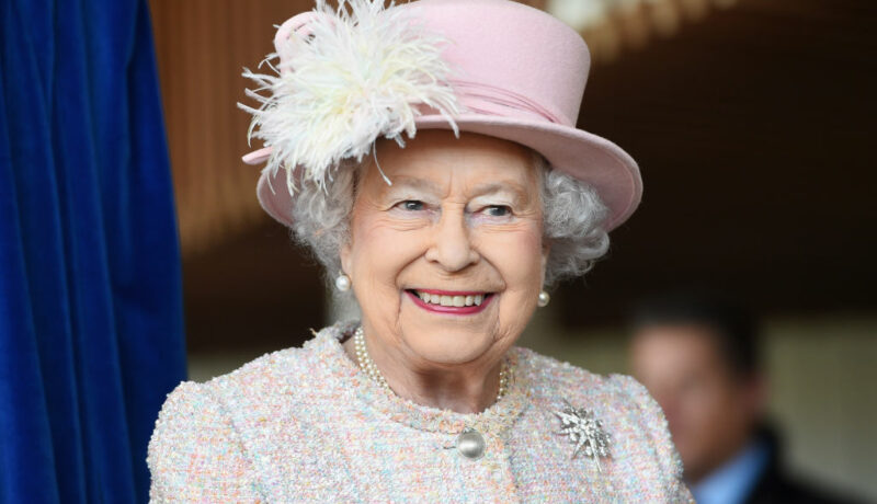 Regina Elisabeta a II-a zâmbind, cu o pășărie roz cu puf pe cap