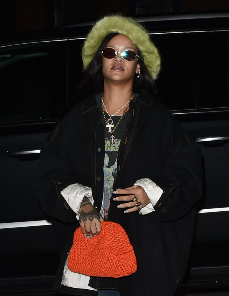 Rihanna, cu ochelari de soare, îmbrăcată cu un tricou cu Metallica, pe care a accesorizat-o cu o părărie verde semnată Emma Brewin și un clutch Bottega Veneta.