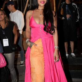 Rihanna într-o pereche de pantaloni stil army de culoare portocalie, cu o rochie lungă și roz pe deasupra