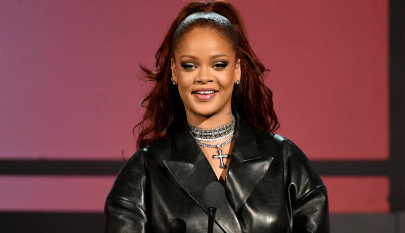 Rihanna într-o jachetă de piele neagră cu părul prins, vorbind pe scenă
