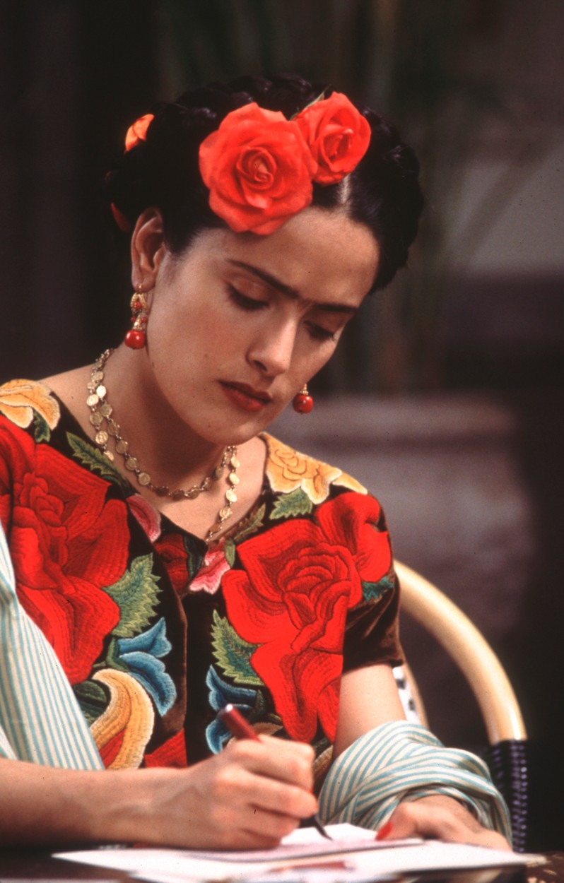 Salma Hayek poartă o costumație Frida Kahlo cu flori roșii în păr și o rochie colorată
